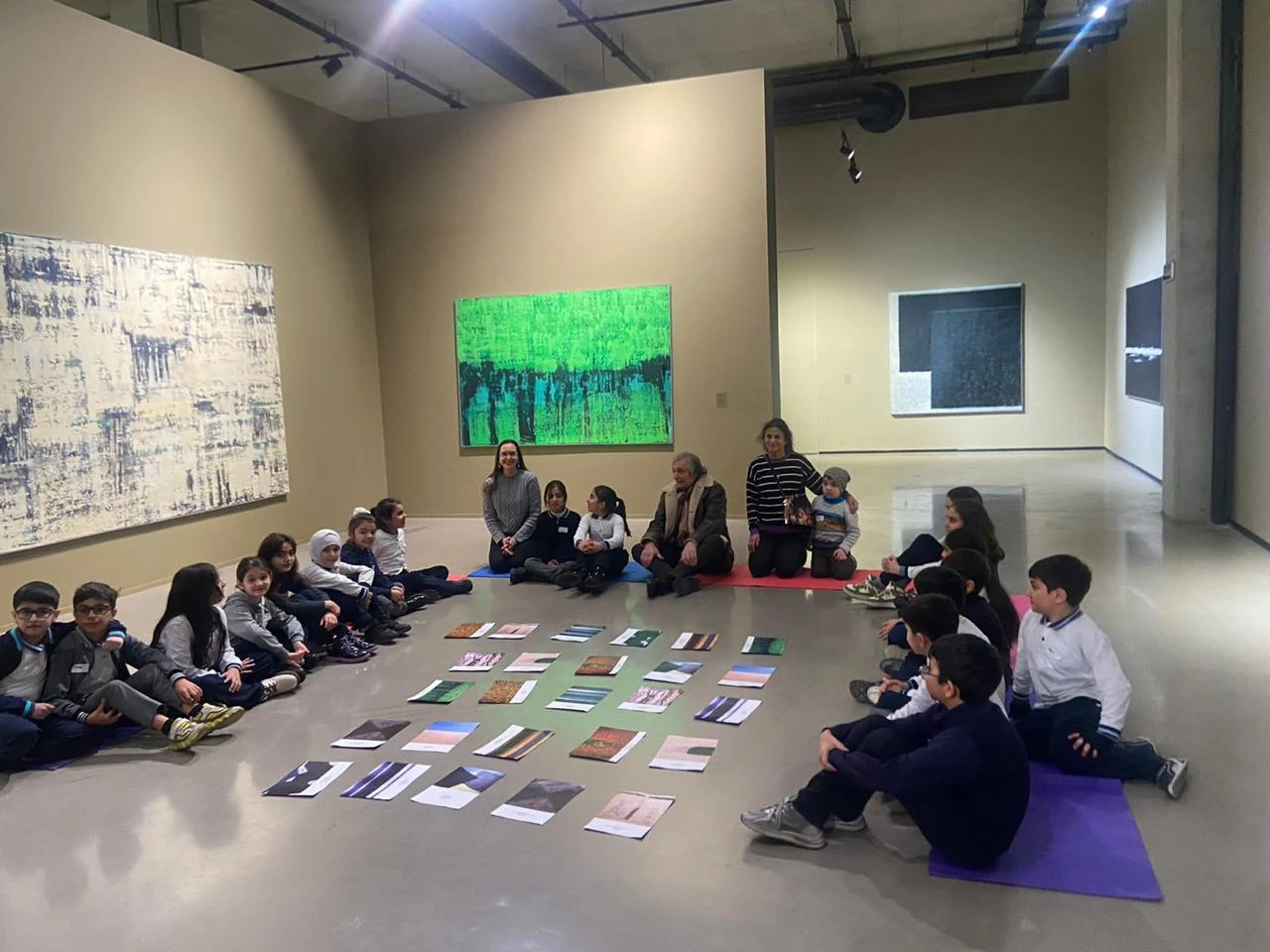 Children and Farhad Khalilov seated in a circle around the children's drawings in the exhibition space.
