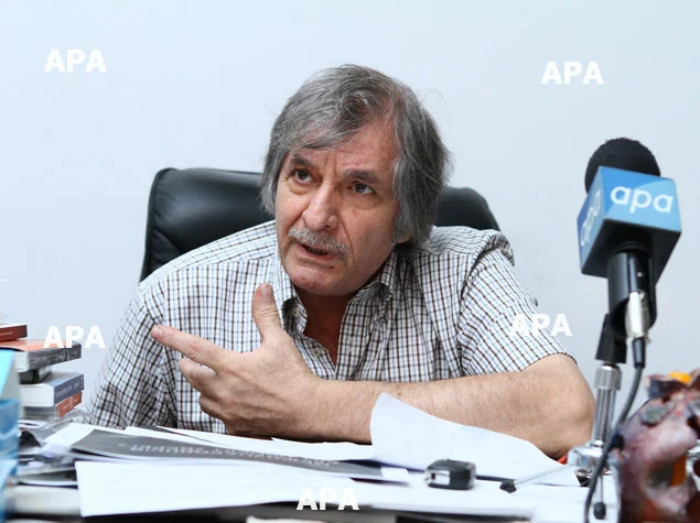 Farhad Khalilov gesturing at his desk beside an APA microphone during the 2014 interview.
