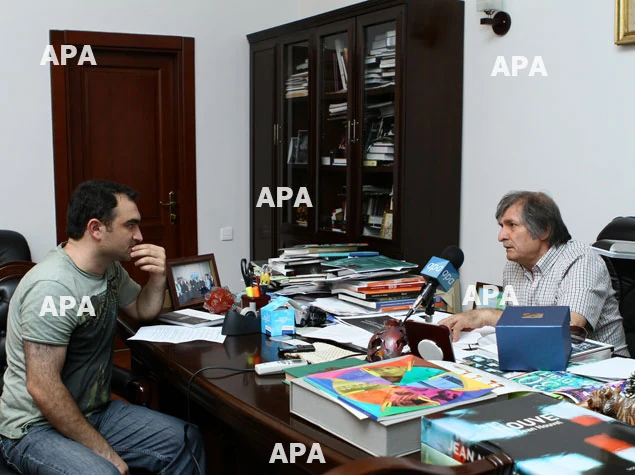 Farhad Khalilov and his interviewer seated across a desk covered with books and papers.