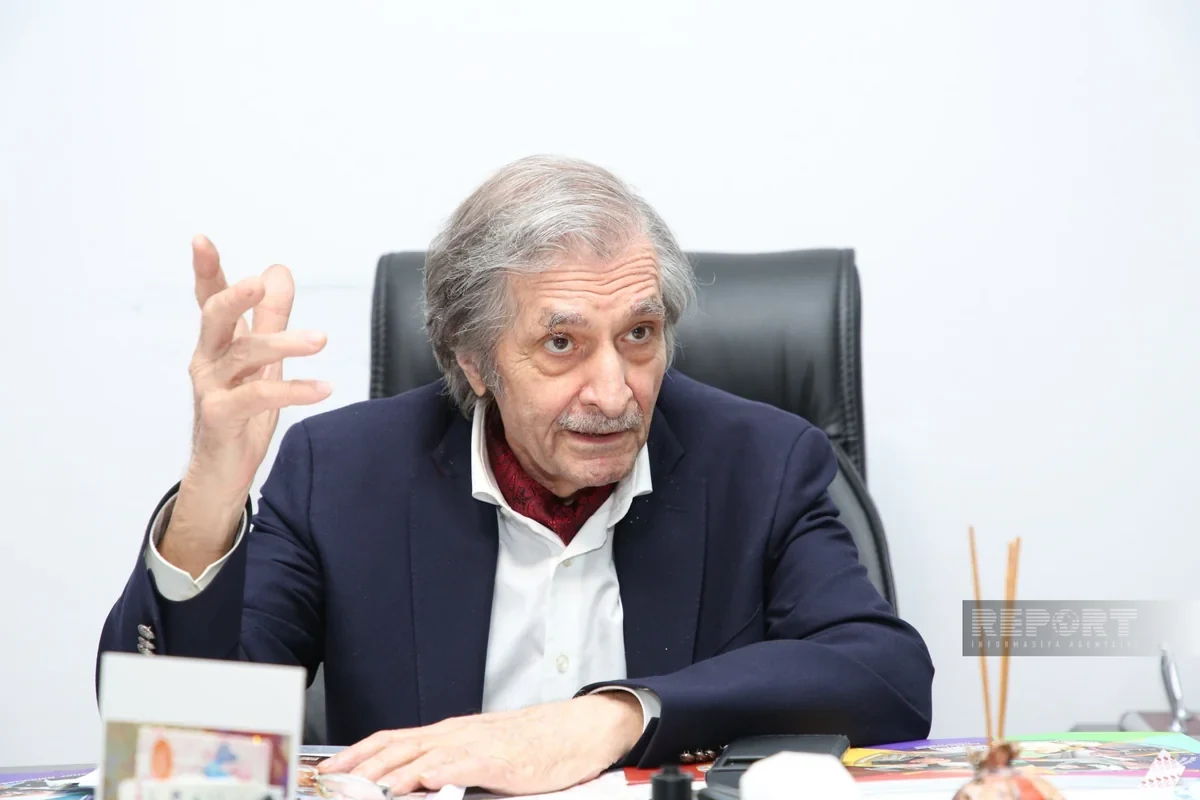 Farhad Khalilov raising his hand while speaking at his desk during the Report.az interview.