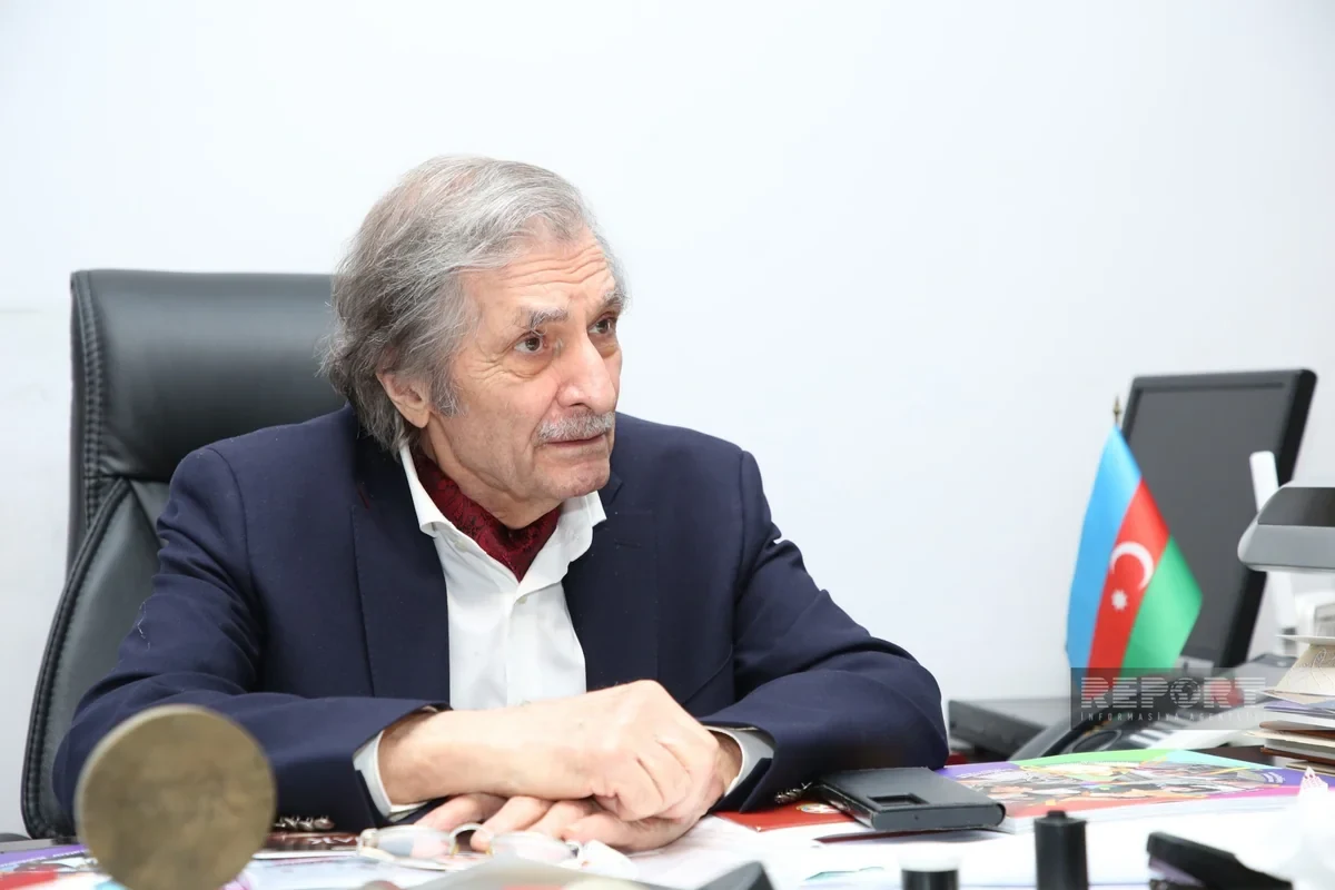 Farhad Khalilov listening during the interview, with an Azerbaijani flag beside his desk.